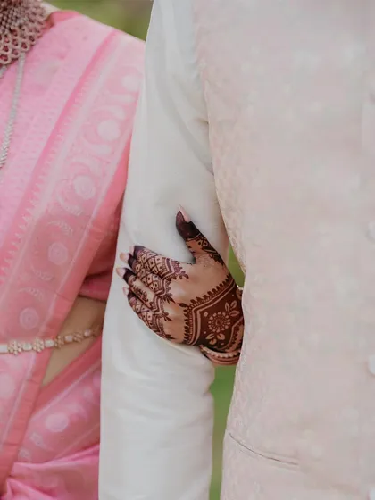 A detail shot focusing on the bride's hand with intricate mehndi resting on the groom's arm, symbolizing their new connection.