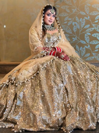 The bride seated, showing the incredible volume and sparkle of this fully sequined golden lehenga.