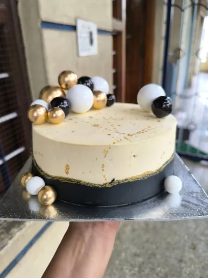 A chic and modern cake in a black, white, and gold color scheme. The design is simple yet striking, with decorative spheres adding a touch of playful elegance.