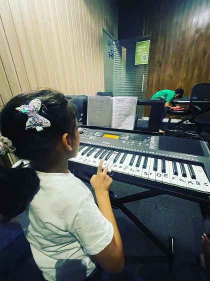 A young girl points to the notes on her keyboard during a lesson, an effective way for beginners to connect written music to the instrument.