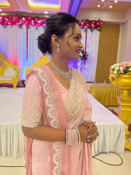A side profile showing the elegant low bun hairstyle, adorned with fresh pink roses to match her saree.