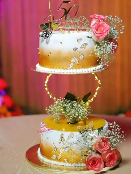 This elegant two-tier spacer cake was designed for a 50th wedding anniversary. The floating design, gold-dusted finish, and fresh flowers create a sophisticated centerpiece for a golden jubilee celebration.