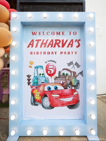 A welcome sign for Atharva's 5th birthday party, featuring Lightning McQueen, Mater, and Luigi, framed with bright marquee lights.