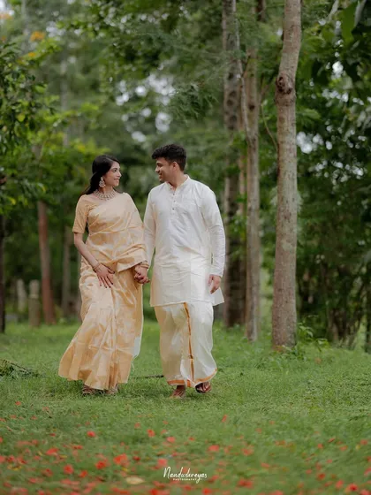 A couple walks hand-in-hand through a wooded area, the path covered in red flowers, creating a romantic and natural scene.