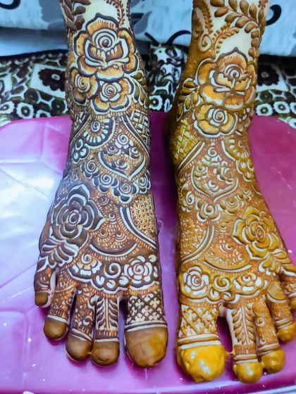A close-up of the fresh henna paste on the feet, showing the 3D texture of the rose patterns.