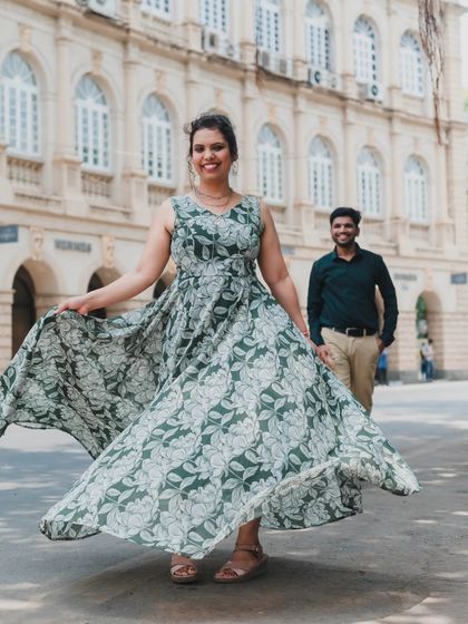 A playful, candid shot with the bride-to-be in the foreground and her partner in the background, set against the elegant facade of a heritage building in Mumbai.