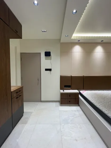 This view of the Sanpada bedroom highlights the seamless integration of the wardrobe and the main door. The clean lines and consistent material palette create a calm and uncluttered environment.