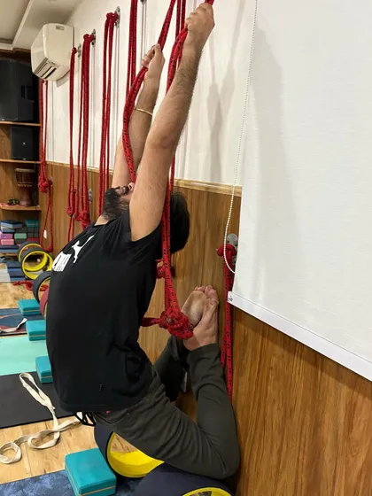 A male student works on his backbend flexibility using the wall ropes and wheel. My classes are for everyone, and props help level the playing field for all body types.