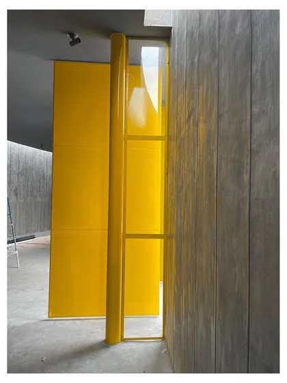 The bright yellow door acts as a beacon within the muted tones of the concrete structure. It is both a functional entryway and a sculptural object, bringing a moment of unexpected joy and color to the memorial space.