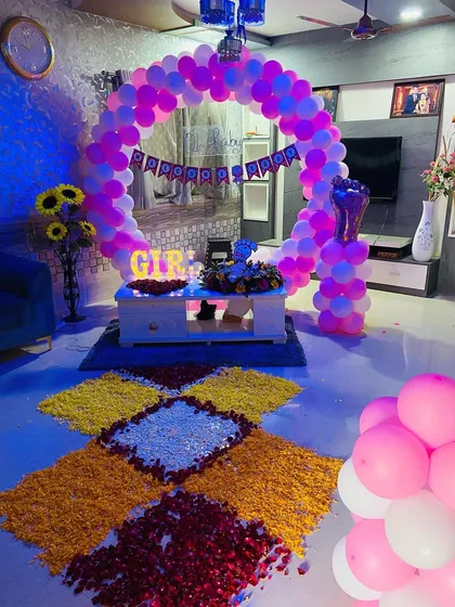 An indoor welcome baby setup with a circular balloon arch, flower rangoli, and 'GIRL' marquee letters.