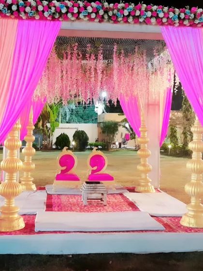 A beautiful pink and white themed mandap for an evening wedding. The structure is decorated with pink drapes, hanging floral strings, and ornate golden pillars.