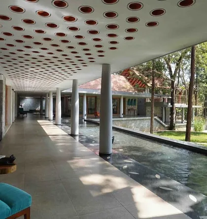 A long, open-air corridor at our resort project guides guests alongside a serene water channel, using columns and a perforated ceiling to create a rhythmic play of light and shadow.