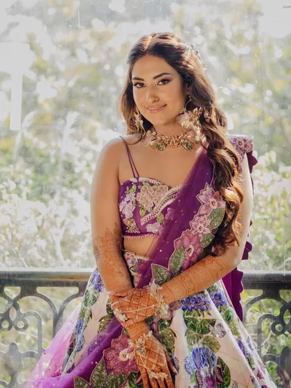 A close-up portrait of the bride, her Mehendi-adorned hands and floral jewelry on full display.