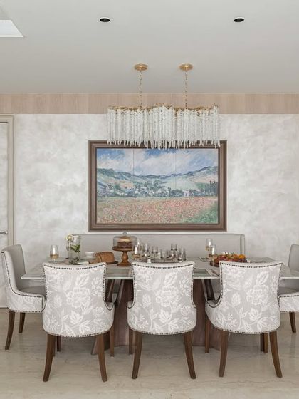 A full view of a dining area designed for elegant entertaining. The patterned chairs and crystal chandelier add a layer of luxury, while the large painting provides a beautiful focal point.