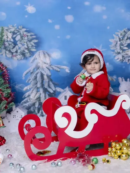 A wide shot of the Christmas sleigh setup, showing the full winter wonderland scene. The baby, dressed as Santa, holds a candy cane, adding to the festive cheer.