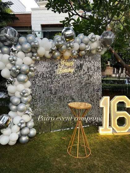 I create chic and modern setups perfect for a 16th birthday or any stylish celebration. This outdoor party features a stunning silver sequin wall for the perfect photo backdrop, a balloon arch with disco ball accents, and large glowing numbers to mark the special age.