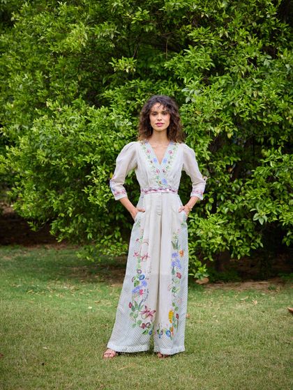 A full-length shot of the embroidered jumpsuit, providing a clear view of the craftsmanship and the relaxed silhouette. The outdoor location enhances the natural feel of the collection.