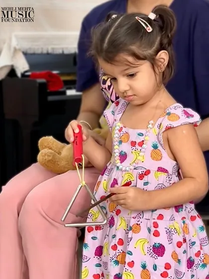 A toddler carefully holds a triangle, ready to make her first sound. These moments of focused exploration are the beginning of a musical journey.