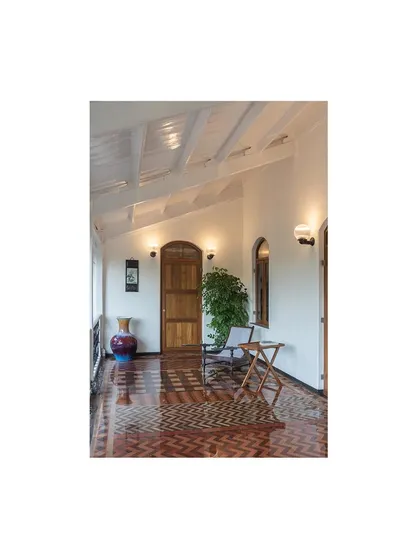 A view down the restored veranda, highlighting the restored wooden door and the intricate tilework. The exposed white-painted roof beams add to the sense of light and space, blending historic and modern aesthetics.