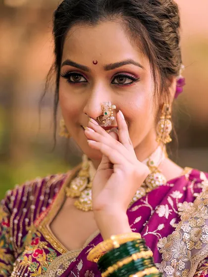 A close-up shot highlighting the beautiful eye makeup and the traditional nath. The soft focus on the background makes the bride's features stand out.