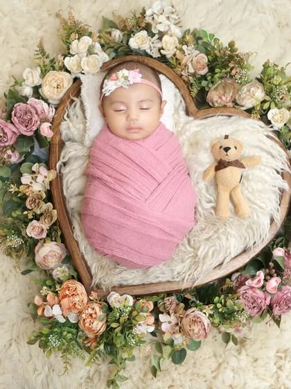 A heart full of love and flowers. This beautiful setup features a baby swaddled in pink, nestled in a heart-shaped basket adorned with a floral wreath.