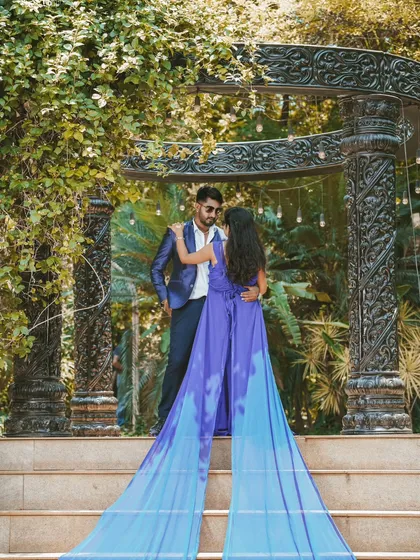 A dramatic and powerful pre-wedding photo. The bride's vibrant blue gown with a long, flowing trail creates a stunning visual against the carved stone backdrop.