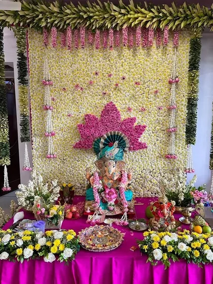 A beautiful floral wall of white flowers serves as the canvas for this Ganpati setup. A pink lotus design and hanging flower strings add a touch of color and traditional elegance.