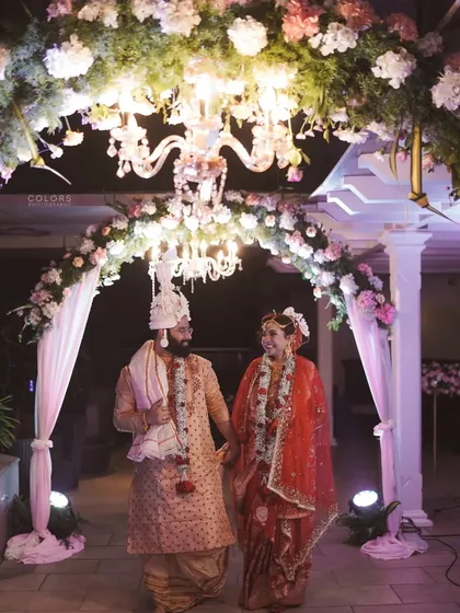 The newlyweds walk hand-in-hand under a beautifully decorated floral archway with a chandelier.