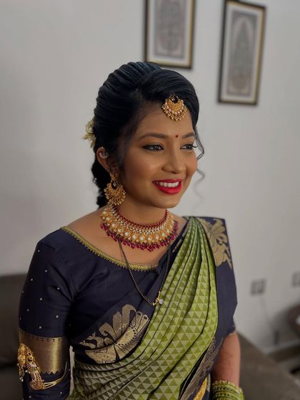 A radiant bridal look with a beautiful red lip that complements the olive green and navy blue silk saree. The hair is styled in a traditional braid, ready for the wedding ceremony.