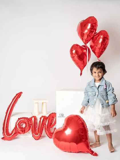A toddler photoshoot with a 'Love' theme, perfect for Valentine's Day or any day. She poses with red heart-shaped balloons and a denim jacket, creating a sweet and modern portrait.