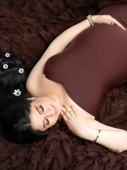 An artistic overhead shot on a textured brown background. The mother-to-be's hair is beautifully arranged with small white flowers, creating a unique and lovely composition.