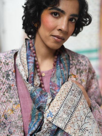 An intimate close-up for Wandering Silk. This shot focuses on the model's expressive gaze and the intricate details of the hand-stitched scarf, highlighting the personal connection to artisanal clothing.