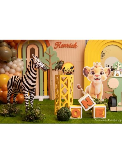 A 'Wild One' first birthday setup featuring a life-sized zebra, a large Simba cutout, and custom 'ONE' blocks. The earthy tones of the balloons and props create a cohesive safari look.