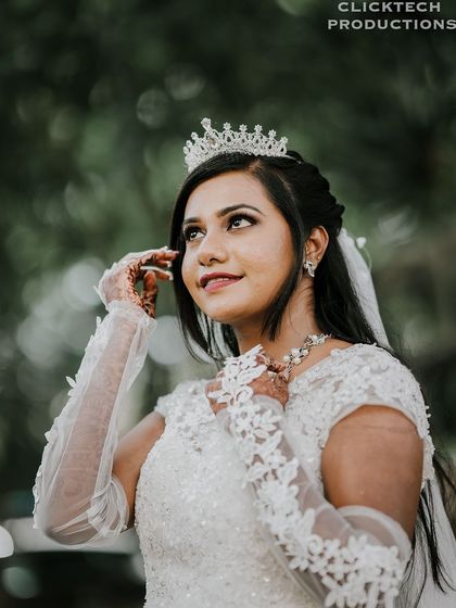 A beautiful close-up of a Christian bride looking up, her portrait framed by lush green foliage. The soft lighting highlights her delicate tiara and lace gloves.