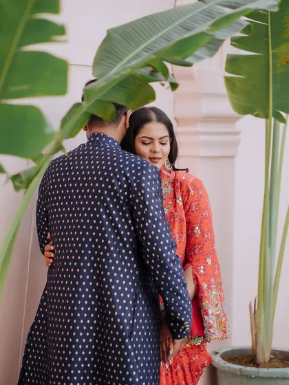 A quiet, intimate moment of a couple embracing, framed by the leaves of a large plant.