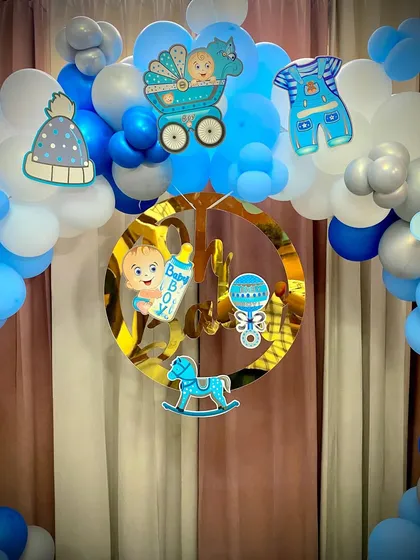 A close-up of the baby boy themed balloon arch, showing the cute cutouts of a rocking horse, rattle, and baby clothes that add a personal touch to the home decor.