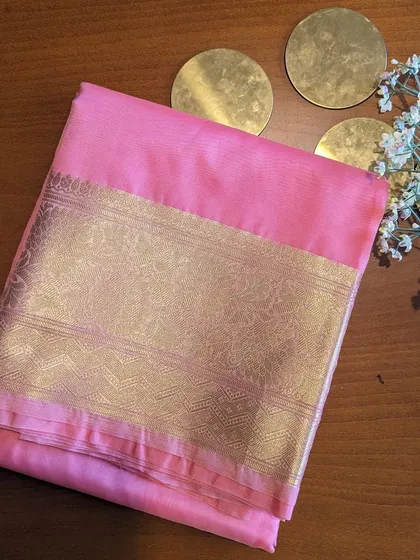 The pink Kora Organza saree is soft and romantic. The wide gold border adds a touch of grandeur to the delicate fabric.