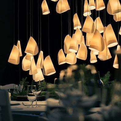 A Bocci 21 installation hangs over a dining table set for a formal dinner, its warm glow creating an elegant and inviting atmosphere.
