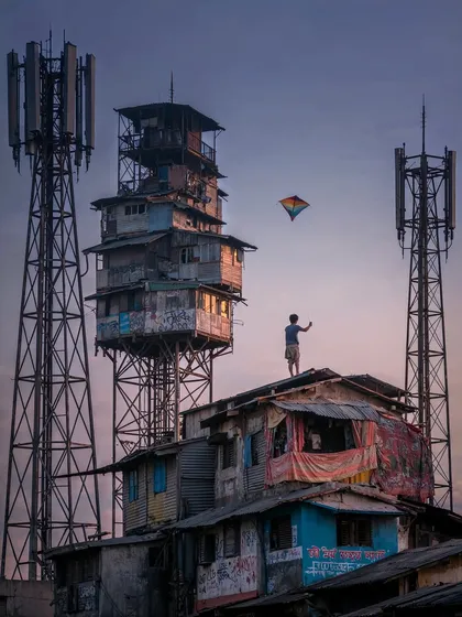 A boy flies a kite from the rooftop of a 'Network Nagar' building at dusk. This image contrasts the dystopian architecture with a timeless, hopeful act of childhood.