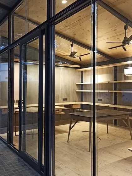 An evening view of the Gazebo office, where the glass walls make the warm, illuminated interior glow, showcasing the balance between the industrial steel frame and the cozy wooden finishes.