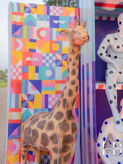 A life-sized giraffe sculpture stands next to the mannequin installation, adding to the surreal and playful menagerie of the carnival.