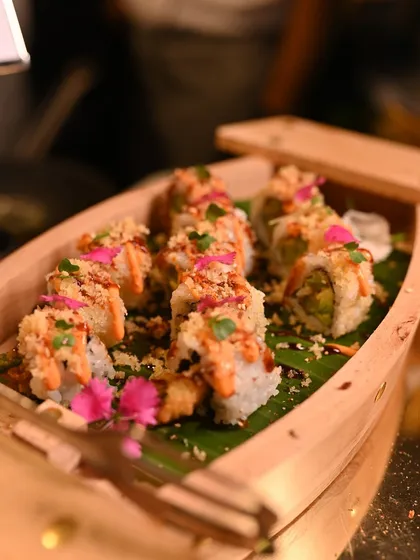 A beautiful wooden boat filled with our Asparagus & Tempura Sushi, topped with crispy bits and edible flowers, ready to be served at our live sushi bar.