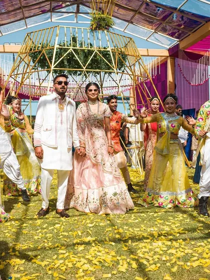 A grand Haldi entry with the couple surrounded by their entire dance troupe. The yellow-themed decor and coordinated outfits create a cohesive and festive look.