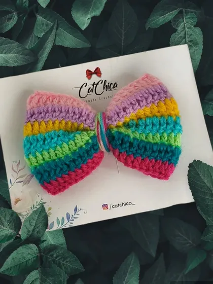 A pastel rainbow crochet bow, perfect for a softer look. I love how this one turned out, pictured here against a background of green leaves.
