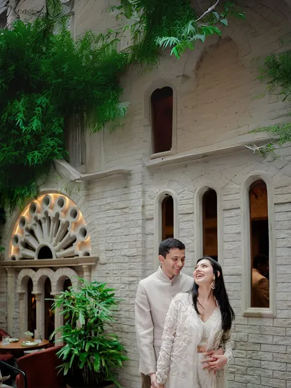A sweet, candid moment between a couple in front of a beautiful stone building with gothic-style windows. Their joyful interaction contrasts beautifully with the classic architecture.