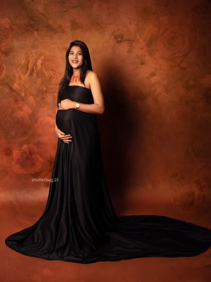 A classic and elegant full-length portrait of an expecting mother in a black satin gown. Her gentle smile and the way she cradles her bump radiate pure happiness and anticipation.