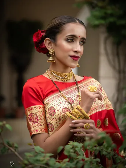 An artistic portrait with the model framed by green leaves, creating a beautiful contrast with her red saree.