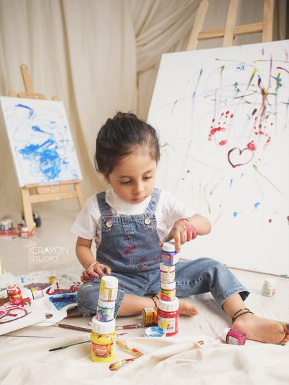 A little artist at work. This toddler is focused on stacking her paint pots during a messy and fun paint-themed session.