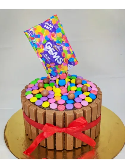 An anti-gravity Gems explosion cake. This chocolate truffle cake is surrounded by KitKats and appears to have Gems pouring out from the packet.