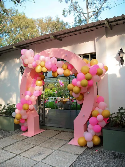 A festive balloon arch at the entrance of The Backyard for a birthday party. The bright pink and gold balloons create a cheerful and celebratory mood.
